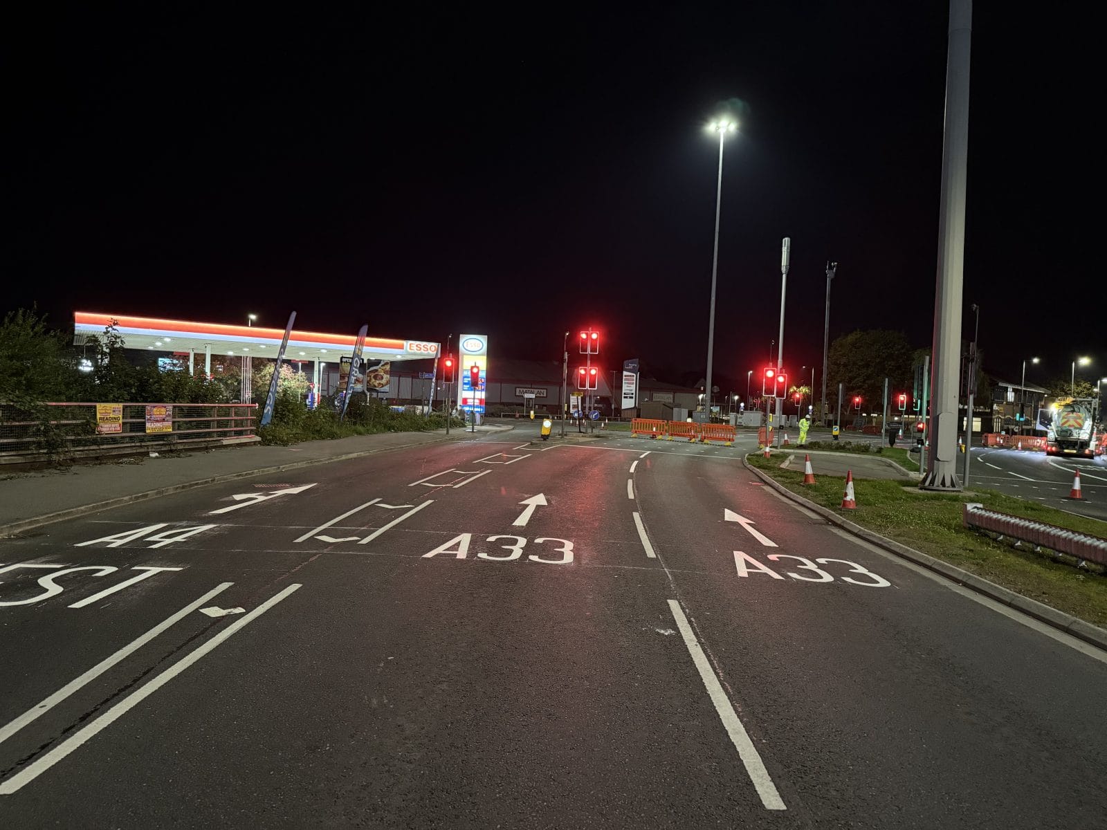 Night road intersection with white road markings and red traffic lights ahead.