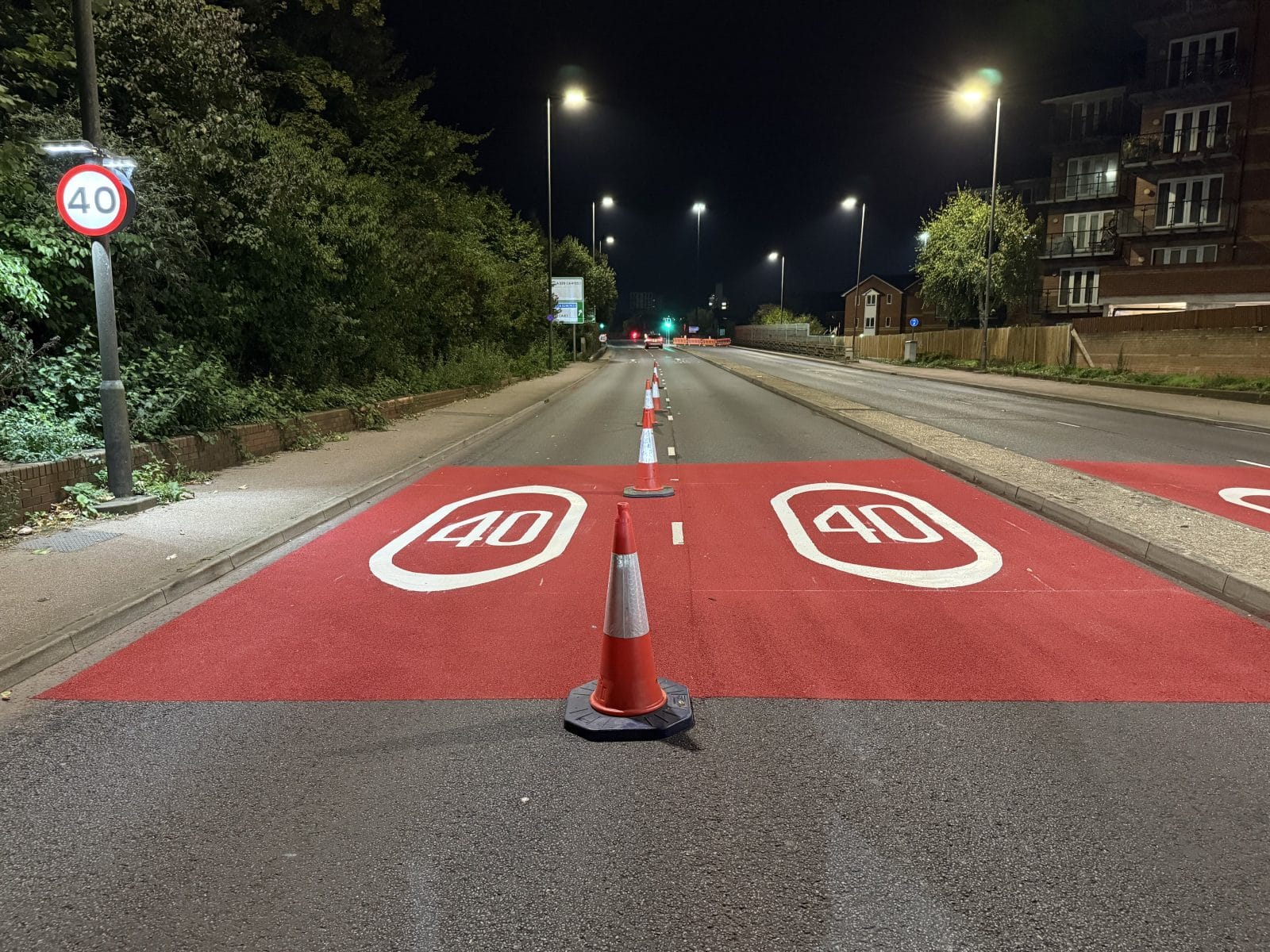 Night road with red speed limit markings and an orange traffic cone in the center.